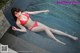 A woman in a red bikini laying on the edge of a pool.