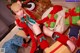 A woman in a santa outfit sitting on the floor next to a pile of presents.