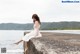 A woman in a white dress sitting on a concrete wall by the water.