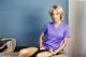 A woman sitting on top of a bed in a purple shirt.