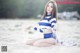 A woman in a blue and white striped top and shorts sitting on the beach.